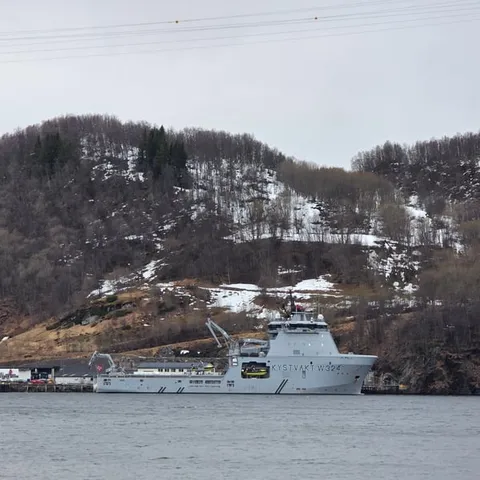A vessel moored below the wooded shore of the fjord