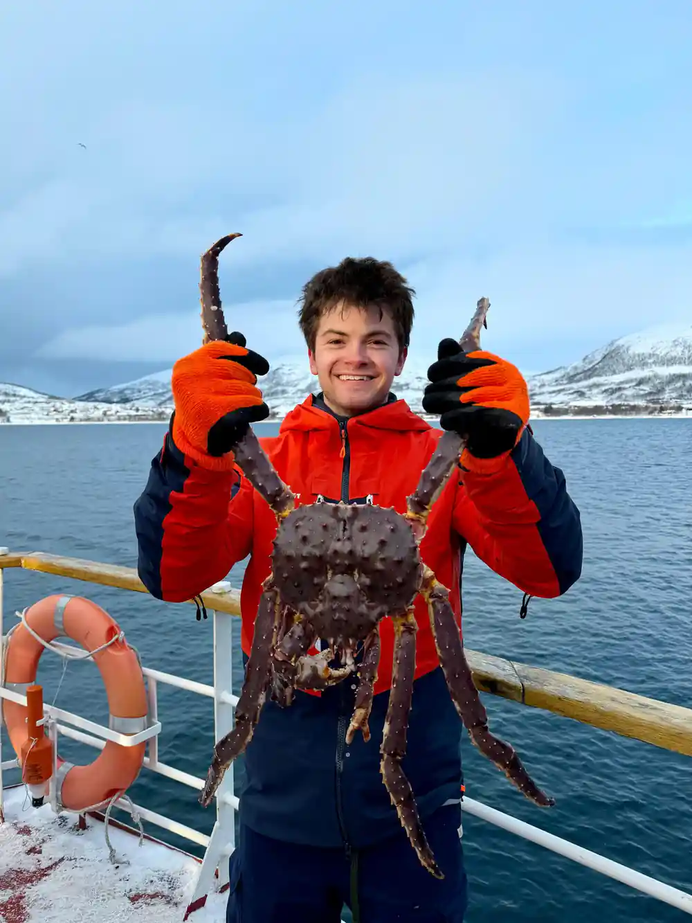 A boy on deck holding a king crab with both gloved hands