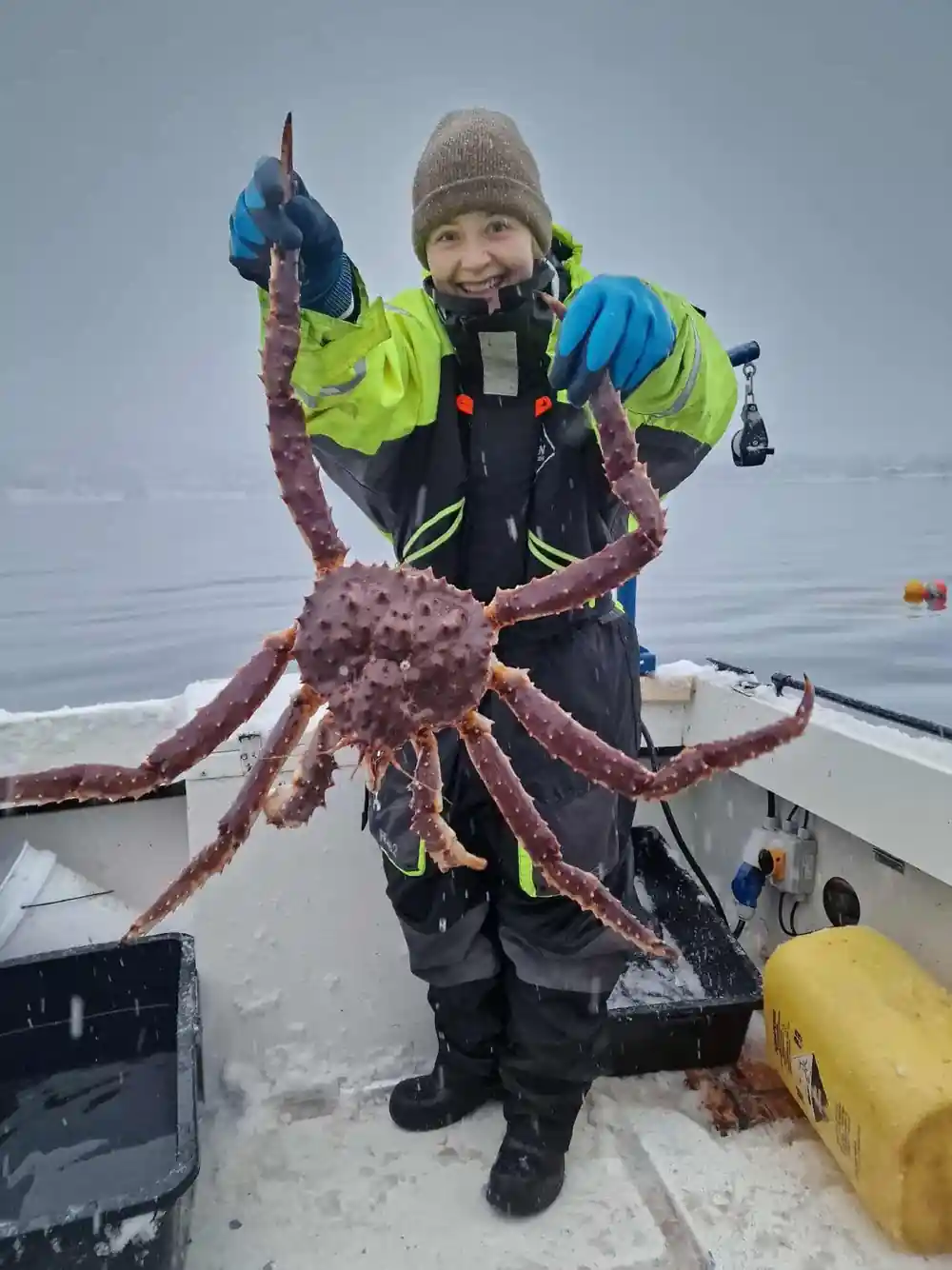 Child in a green flotation suit holding a king crab aloft on deck