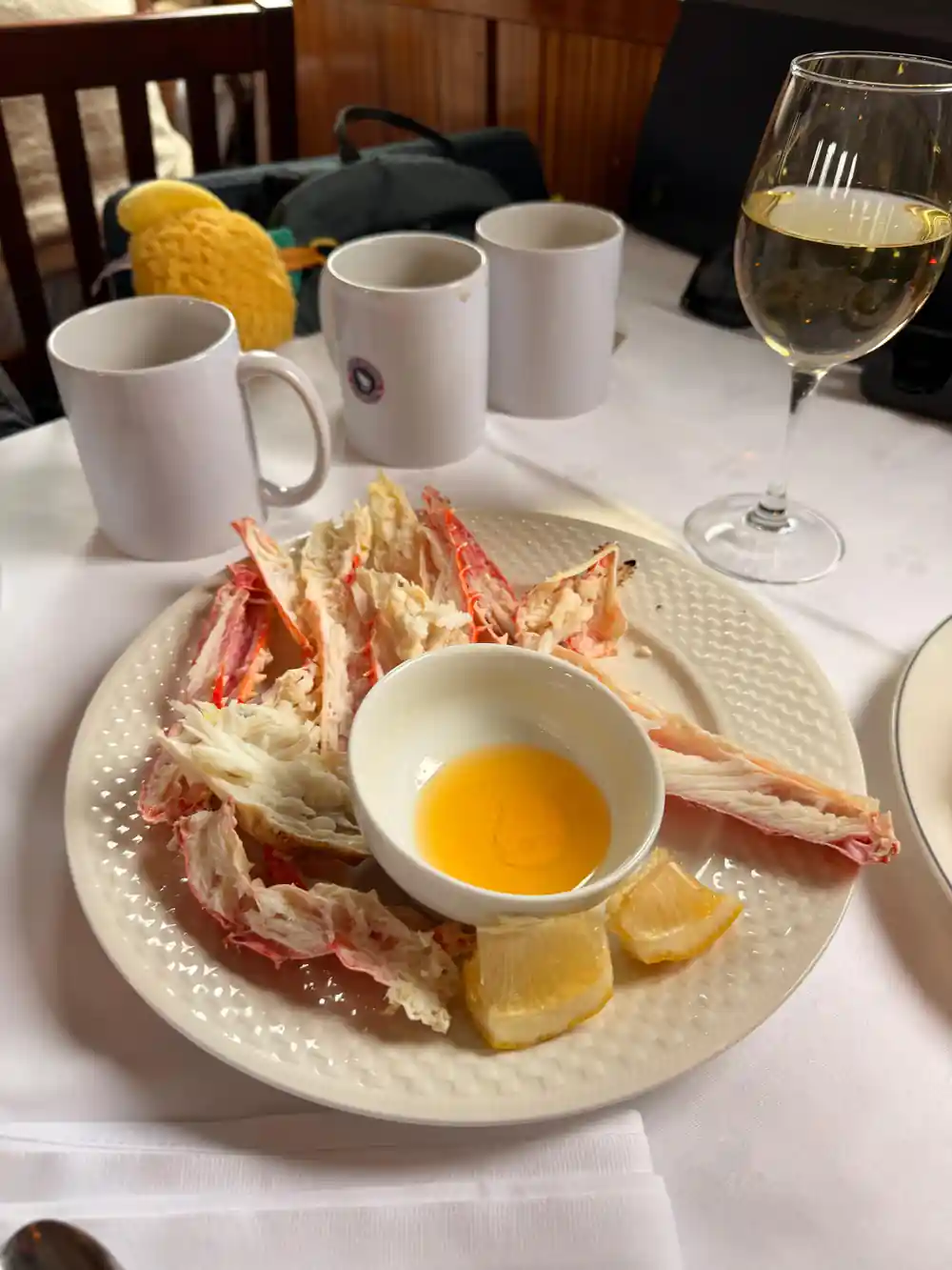 Crab legs on a plate with melted butter, mugs and a wine glass