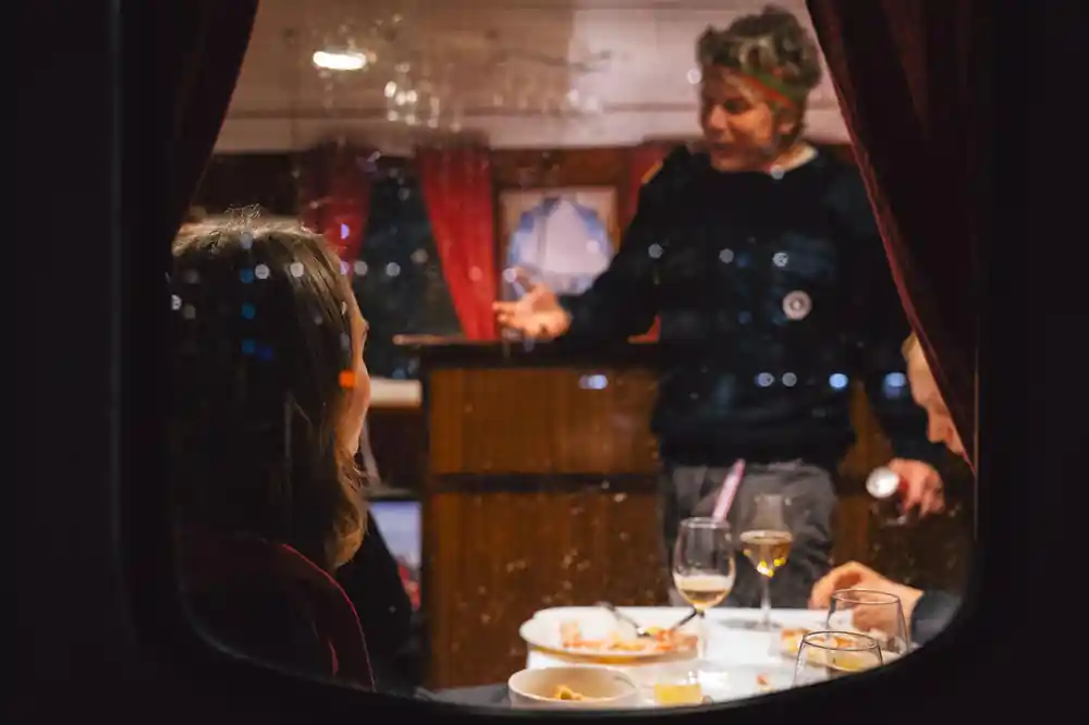 Crew member talking to seated guests at a table in the saloon