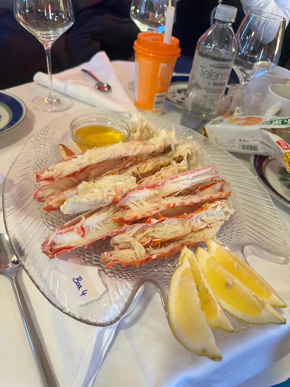 A glass platter of crab legs with lemon wedges and butter