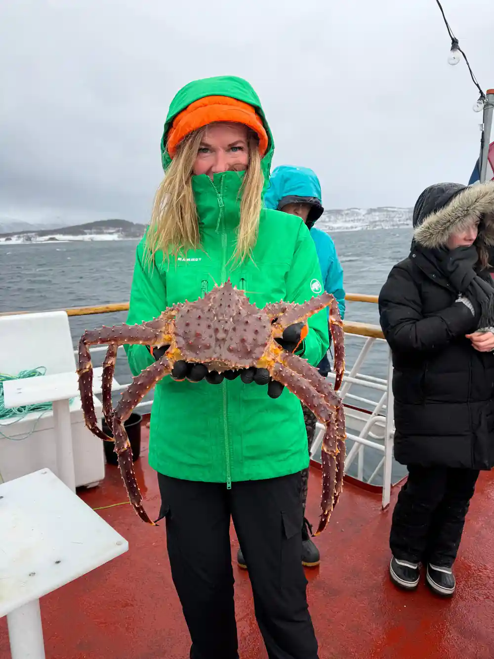 Guest in a green jacket holding a king crab in front of her on deck