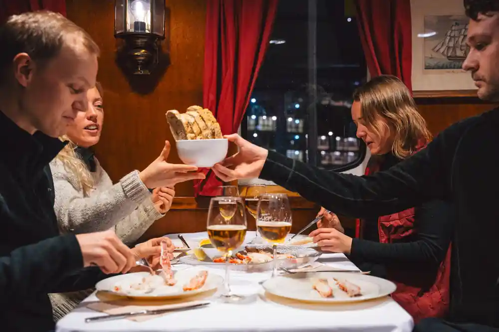 Guests passing a bowl across a table set with crab and glasses