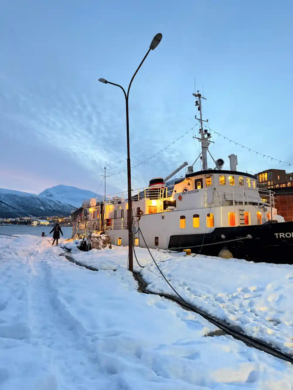 The lit vessel moored at a snowy quay at dusk