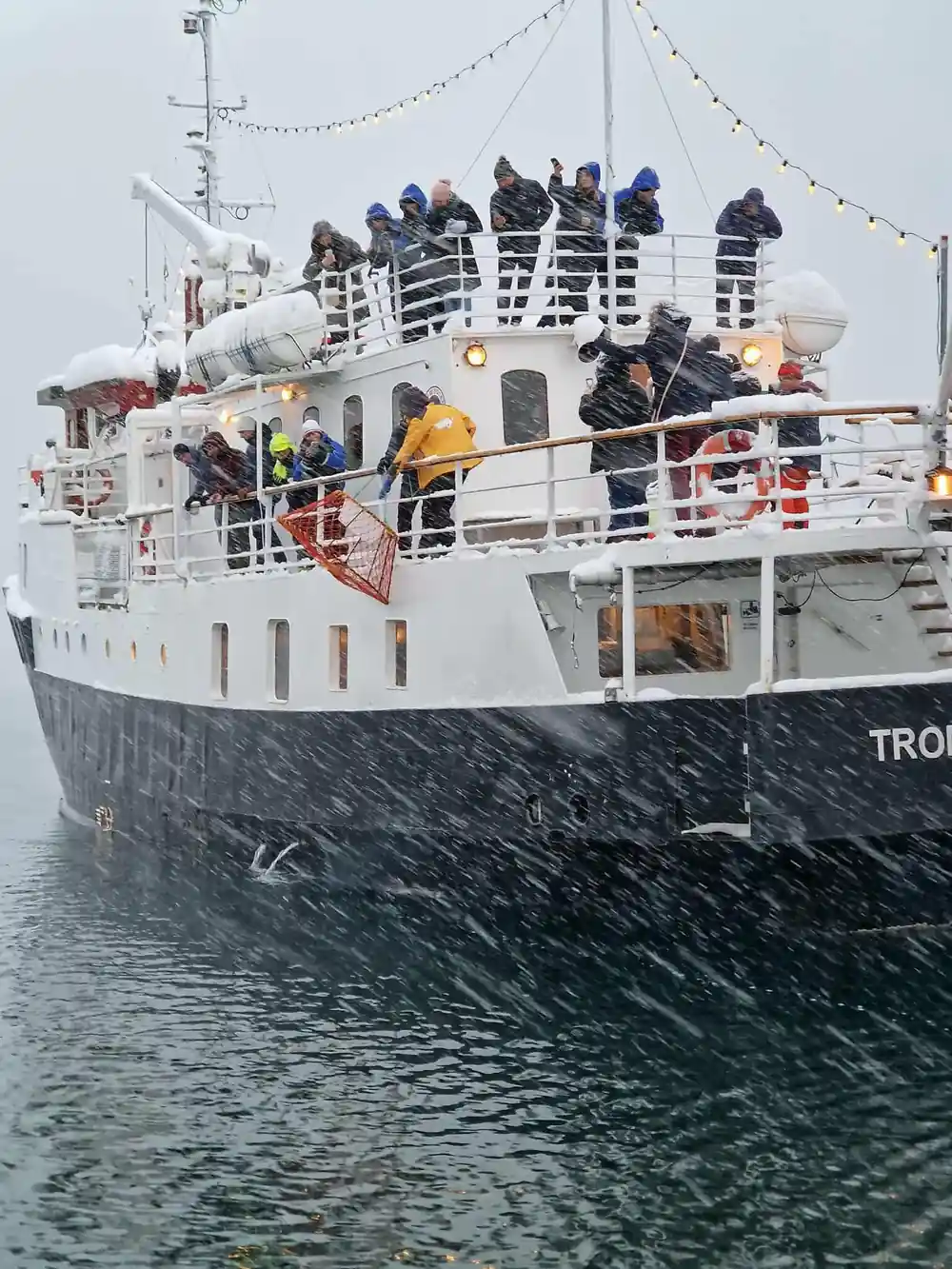 Passengers lining the rail of the vessel in falling snow
