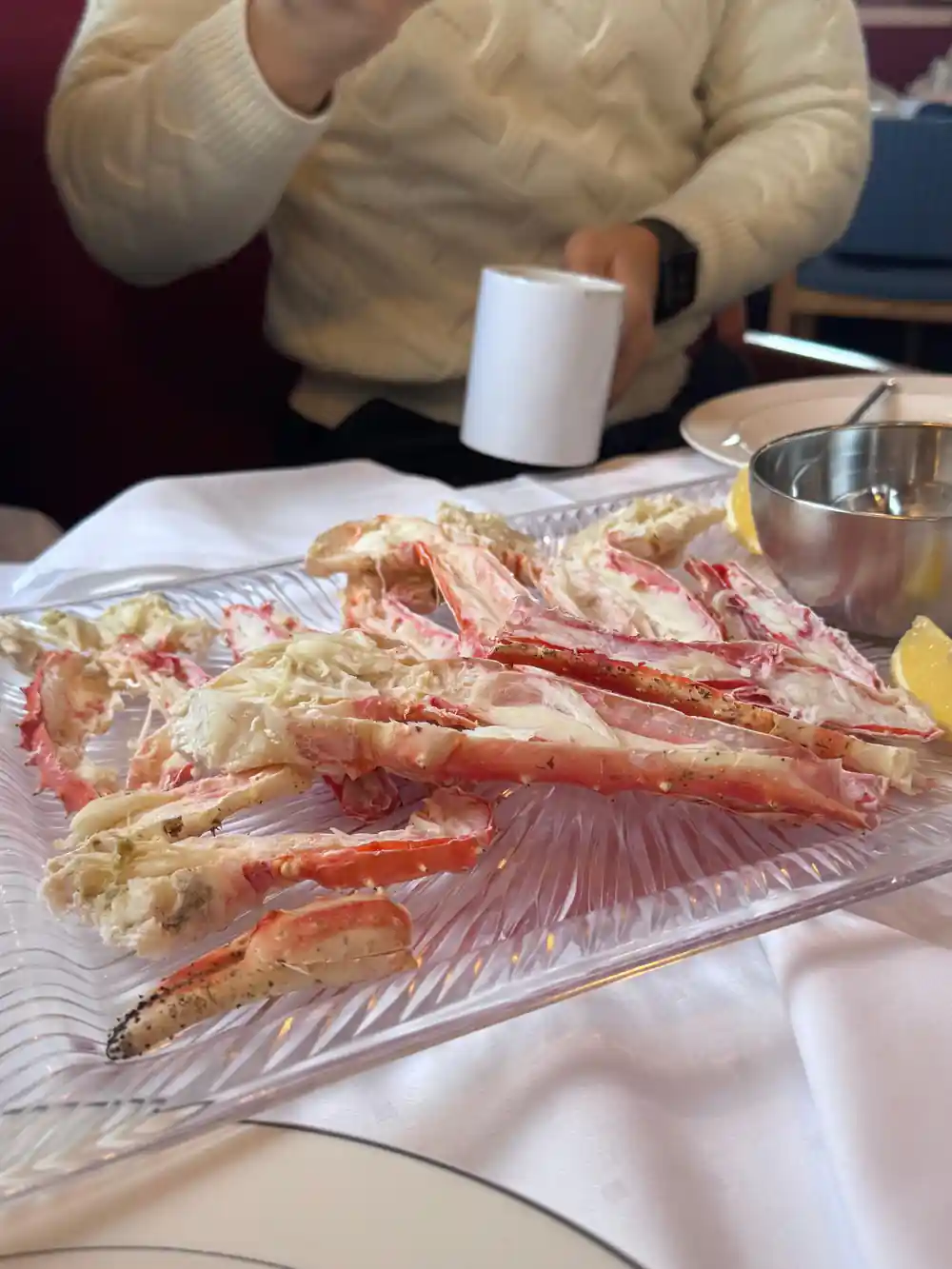 A platter of crab legs on a white cloth with a guest behind