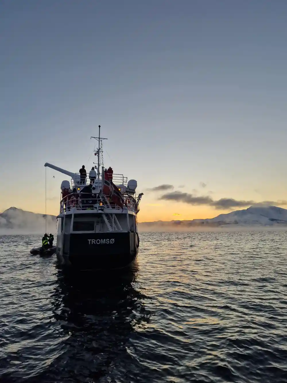 The vessel at anchor on calm water under a low winter sun